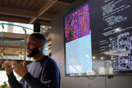 Man gives presentation with screens behind him displaying coding