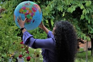 Woman with long curly black hair in forested setting, looking of at large globe held high in her hands