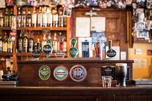 A typical bar in a UK pub, stocked with various ales on tap and bottles stacked in rows behind.