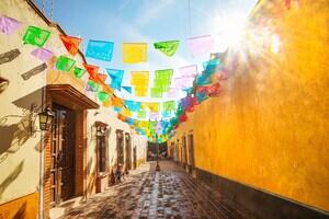 A colourful Spanish street with flags hanging across, lit by the sun in a blue sky.