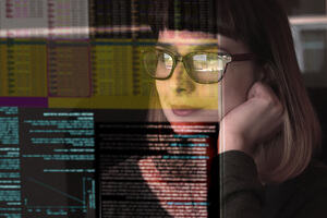 A woman with glasses observes data on a computer screen.