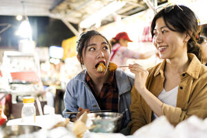 2 friends trying different street foods at night market in Taiwan.