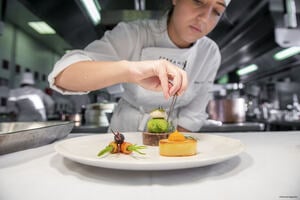 Close-up of a chef plating up plate of French cuisine in a restaurant kitchen.