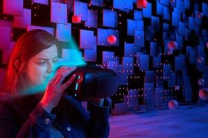 Woman looking into a VR headset against a futuristic backdrop of squares and floating circles.