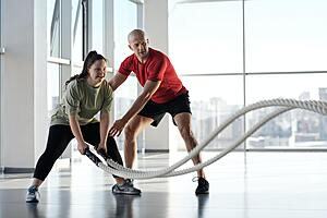 A woman training with ropes whilst a man supports and views her form