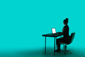A woman sits at a desk on a computer with a blue background.