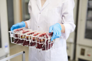 Medical professional carrying a tray of bagged blood in a laboratory