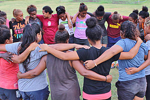 Chicas conectadas en círculo, uniendo sus brazos entre ellas alrededor de su espalda.