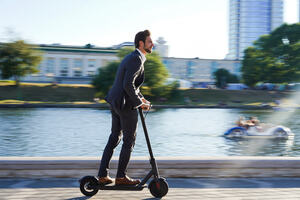 Man in business suit riding scooter along river