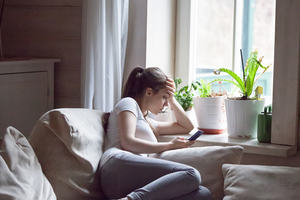 A teenage girl sits by the window, looking at her mobile phone, head in her hand
