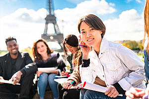 A group of young people, from a variety of international backgrounds, studying with pens and pads. The Eiffel Tower is in the background.