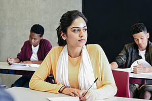 Young woman in university class, thinking and writing 